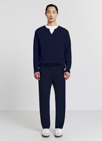 Pull en maille bleu marine avec un col en V et détail de bouton, associé à un pantalon bleu marine à taille élastique et des baskets blanches. Design simple et décontracté.