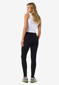 Črne legice z visokim pasom, izdelane iz elastičnega materiala, z zadnjimi žepi in gladko teksturo, nosijo se z oprijetim belim topom brez rokavov.