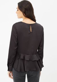 Blusa negra de manga larga con un dobladillo con volantes y un escote redondeado, que presenta un pequeño detalle en forma de ojal en la parte posterior. Material sedoso.
