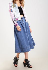 Lekki, pastelowy bomber z haftem, w połączeniu z niebieską dżinsową spódnicą. Czarne odkryte botki na obcasie dopełniają całość.