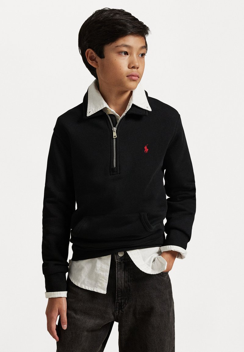 Felpa nera con mezza zip, con un colletto bianco a contrasto e un logo rosso sul petto, abbinata a una camicia bianca sotto.