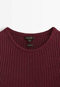 Burgundowa sweter w prążki z okrągłym dekoltem i subtelną pionową teksturą. Metka wskazuje rozmiar i miejsce produkcji, wykonany w Turcji.