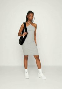 Vestido mini cinza, sem mangas, com decote diagonal. Combinado com sapatilhas brancas e uma mala de ombro preta. Design simples e justo.