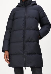 Laivastonsininen toppatakki hupulla, jossa on tikattuja osioita, täysi vetoketju ja sivutaskut. Valmistettu sileästä, vedenkestävästä materiaalista.