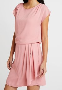 Rosa klänning med korta ärmar i lätt tyg, med en plisserad kjol och avslappnad passform. Slät textur, rund halsringning och knälängd.