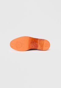 Παπούτσι επίσημο με δερμάτινη σόλα, φαίνεται από κάτω, παρουσιάζοντας γυαλιστερή πορτοκαλί σόλα με ανάγλυφο λογότυπο και καρφιά στη φτέρνα.