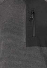 Graues Stoffhemd mit einer schwarzen Reißverschlusstasche auf der Brust. Die Textur ist glatt mit einem kontrastierenden matten Bereich um die Tasche.