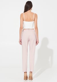 Top blanc court avec des bretelles spaghetti associé à un pantalon ajusté rose clair. La tenue se caractérise par des textures lisses et un design minimaliste.