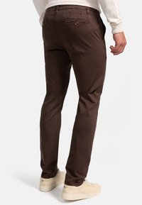 Pantalones de algodón marrones con corte slim, que cuentan con bolsillos traseros, una textura sutil y que se complementan con calzado de colores claros.