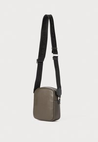 Borsa a tracolla verde oliva in pelle liscia, caratterizzata da una forma rettangolare, chiusura con zip e tracolla nera regolabile con testo del logo.