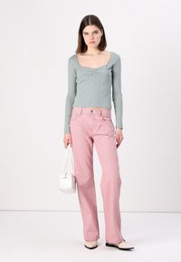 Vaaleanvihreä ribbipintaista pitkähihaista puseroa, jossa on avara kaula-aukko, on yhdistetty vaaleanpunaiseen raidalliseen leveälahkeiseen housuun. Mallilla on mukanaan pieni valkoinen käsilaukku.