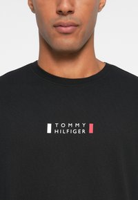 Μαύρο κοντομάνικο μπλουζάκι με λευκό και κόκκινο λογότυπο "TOMMY HILFIGER" στο κέντρο, με στρογγυλή λαιμόκοψη και μαλακή βαμβακερή υφή.