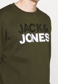 Felpa verde oliva con testo in bold nero e bianco "JACK & JONES" in diverse dimensioni; scollo rotondo e texture morbida.