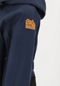 Marinblå huvtröja i en texturerad tyg, med en framträdande läderlogotyp i brunt som har ett bergsmotiv och texten "1991 SWEDEMOUNT".