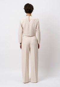 Beige op maat gemaakt tweedelig pak met een cropped top met een keyhole aan de achterkant en hoge taille wijde pijpen broek; gladde textuur, strakke lijnen.
