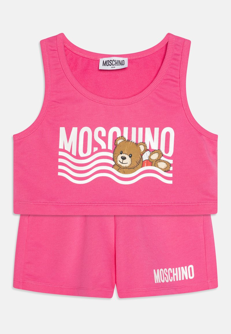 Roza pamučna dvodijelna odjeća koja se sastoji od majice bez rukava s grafikom medvjeda i tekstom "MOSCHINO", u kombinaciji s odgovarajućim kratkim hlačama.