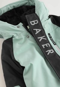 Mentovo zelená a čierna zimná bunda s plyšovým čiernym podšívkou, zdobená výrazným logom "BAKER" a zipsovými vreckami.