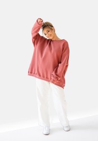 Oversized, długoslewy sweter w różowym polaru; okrągły dekolt, ściągacze u rękawów i luźny krój, zestawiony z białymi szerokimi spodniami i trampkami.