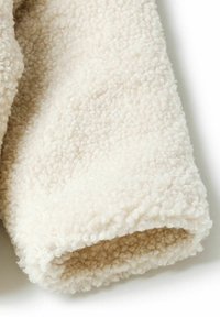 Off-white polārfleece audums ar mīkstu, teksturētu virsmu un nedaudz pūkainu izskatu. Iezīmēts ar velmētu apmalīti.