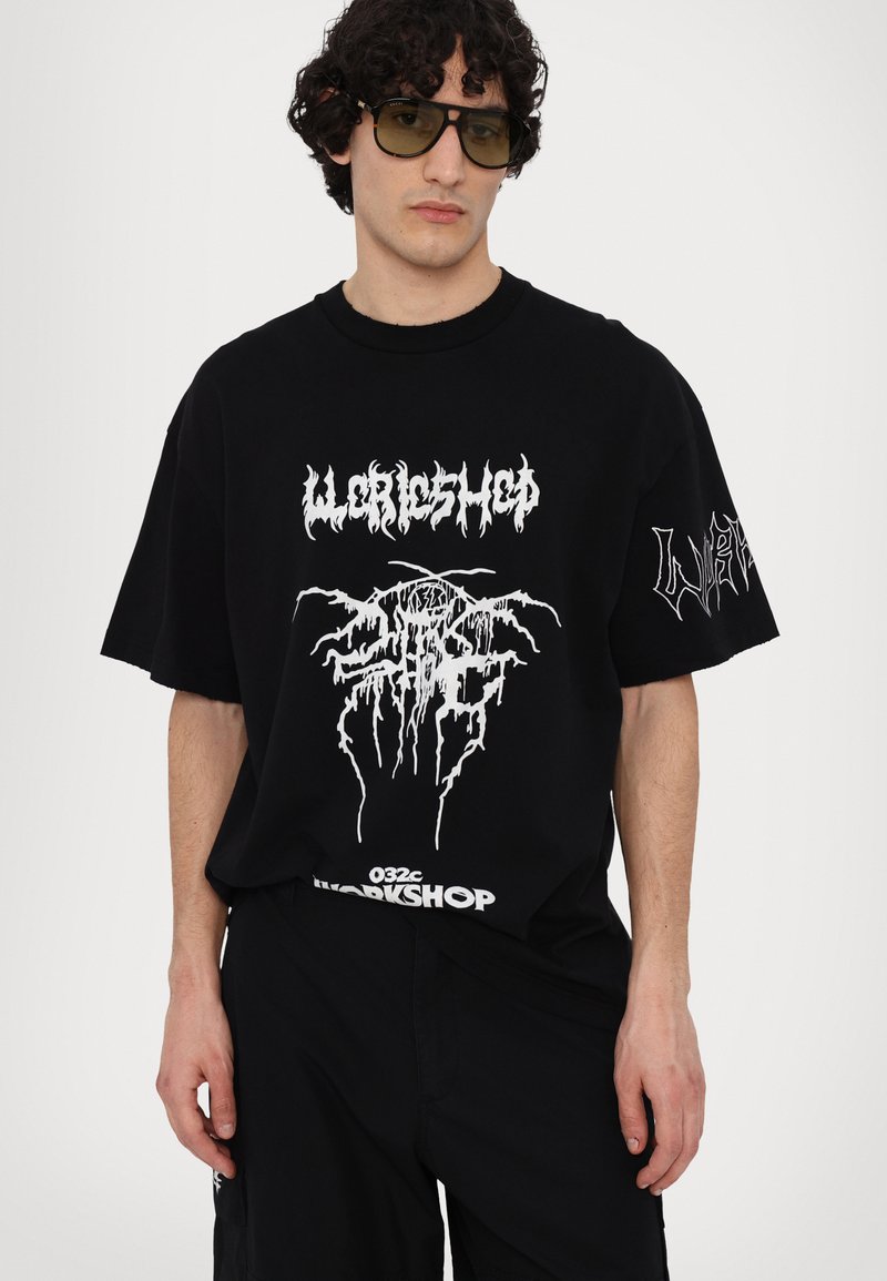 Sort oversized T-shirt med hvid grafisk tekst og design på fronten og ærmet. Lavet af bomuld, med rund hals og korte ærmer.
