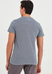 T-shirt grigio a maniche corte con scollatura rotonda, tessuto testurizzato e maniche arrotolate. L'orlo è leggermente curvato con un piccolo etichetta sul lato.