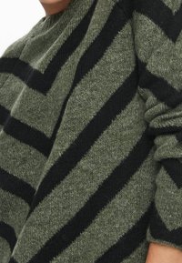 Pull vert avec de larges rayures diagonales noires, fabriqué en tissu tricoté texturé, coupe décontractée et poignets côtelés.