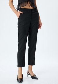 Zwarte op maat gemaakte broek met een gladde textuur, voorzien van zijzakken en een slim fit. Gecombineerd met glanzende zwarte hakken.