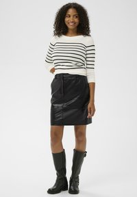 Raidallinen mustavalkoinen neulepaita yhdistetty mustaan nahkahameeseen ja polven yli ulottuviin mustiin saappaisiin. Sileä nahkatexture; kapea malli.