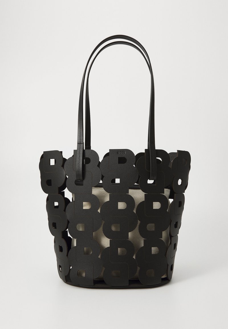 Black tote bag made of cut-out leather, featuring a mesh interior. Two long handles and a structured shape highlight the modern design.