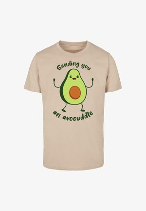 Beżowa bawełniana koszulka z kreskówkowym awokado z rękami, brązowym pestką oraz napisem "Wysyłam ci awokadowe przytulenie" na zielono.