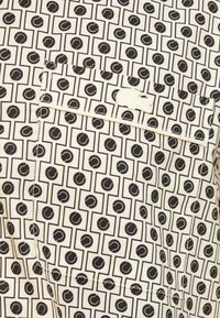 Korte mouwen shirt van crèmekleurige stof met een zwart geometrisch patroon en cirkelaccenten. Inclusief een borstzak en gestikte details.