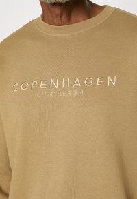 Sweatshirt beige en coton avec col rond. Présente un texte brodé "COPENHAGEN LINDBERGH" en fil contrastant sur la poitrine.
