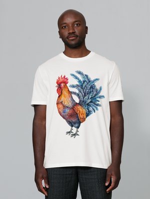 White t-shirt featuring a colorful rooster graphic with blue foliage accents. Short sleeves and a round neckline.