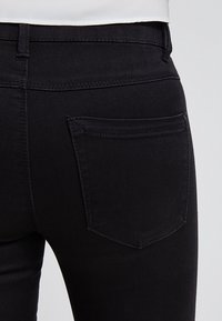 Jeans de mezclilla negra con un diseño ajustado, que cuentan con un único bolsillo trasero y detalles de costura sutiles a lo largo de la cintura y los bordes del bolsillo.