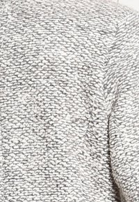 Grijs gestructureerde stof met een geweven patroon, met een zachte, enigszins grove oppervlakte. Het ontwerp is een mix van lichte en donkere grijze vezels.