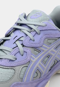 Lichtpaars sportieve schoen met grijze accenten, meshstof, gestructureerde overlays en contrasterende veters; heeft een afgeronde neus en een gevoerde zool.