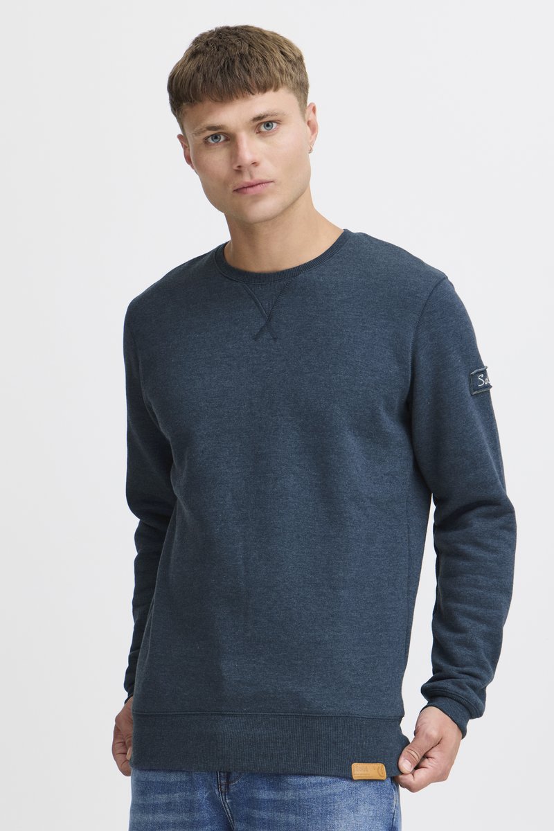 Sudadera azul marino hecha de una tela suave, con un cuello redondo, mangas largas y una etiqueta tejida como acento en el dobladillo.
