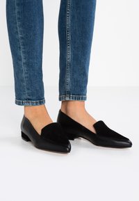 Černé polobotky s špičatou špičkou, se zamykovým zdobením na nártu a nízkým blokovým podpatkem. Nosené s ohrnutými modrými džíny.