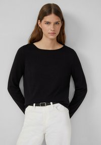 Zwarte longsleeve top met een wijd uitgesneden halslijn, gemaakt van zacht breigaren, gecombineerd met witte jeans en een zwarte riem met geperforeerde details.