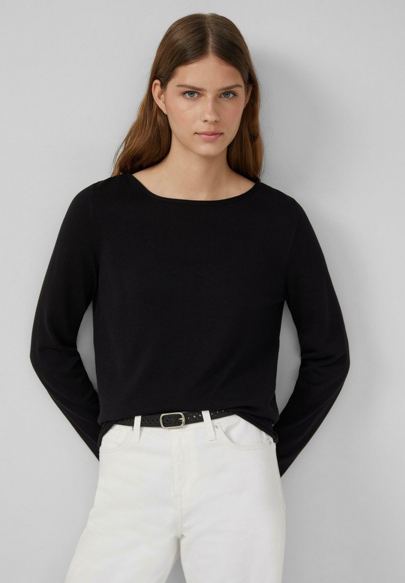 Zwarte longsleeve top met een wijd uitgesneden halslijn, gemaakt van zacht breigaren, gecombineerd met witte jeans en een zwarte riem met geperforeerde details.
