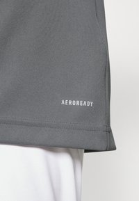Camiseta atlética gris hecha de una tela texturizada, con un dobladillo recto y un sutil logo blanco "AEROREADY" en el lado inferior.