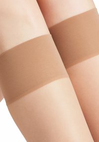 Bruine bovenbenen sokken met een gladde textuur en een brede band aan de bovenkant rusten tegen lichte huid en tonen een naadloos ontwerp.