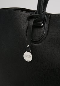 Sac à main en cuir noir texturé avec une bandoulière nouée et une étiquette ronde en métal argenté gravée de "L.CREDI MUNICH."