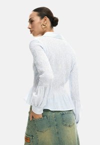 Valge ja siniste triipudega pluus, millel on kujundatud vartus, peplum-ääris ja lainevad varrukad, kantud teksaseelikuga, millel on taskud.