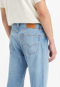 Light blue denim jeans featuring a relaxed fit, subtle fading, and a brown leather patch with branding at the back waist.