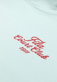 Lichtblauwe stof met rood cursief tekst "Fila Court Club 1911" erop gedrukt.