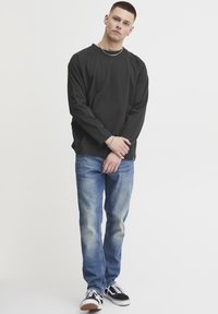 Black long-sleeve shirt with a relaxed fit, paired with light blue faded jeans and black sneakers with white laces. Simple design elements.