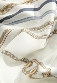 Zijden sjaal met een witte achtergrond en patronen van gouden kettingen en gespen. De stof is glad met een licht glanzende textuur.