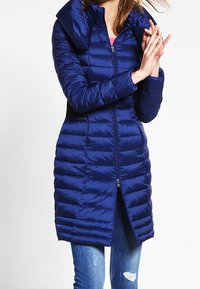 Navyblauwe gewatteerde jas met een hoge kraag, ritssluiting aan de voorkant en verticale stiknaad. Draag het over een spijkerbroek, met een middellange snit en een strakke uitstraling.