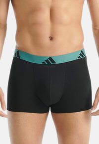 Črne bokserice s širokim turkiznim elastičnim pasom, ki vsebuje črne logotipe Adidas; gladka tkanina, prilegajoča se oblika.